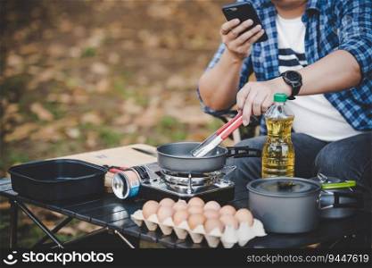 Asian traveler man glasses frying a tasty fried egg in a hot pan at the campsite. Outdoor cooking, traveling, camping, lifestyle concept.