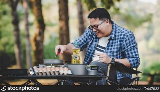 Asian traveler man glasses frying a tasty fried egg in a hot pan at the c&site. Outdoor cooking, traveling, c&ing, lifestyle concept.