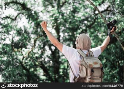 Asian traveler man with backpack holding a camera and making a happy gesture in forest with copy space. Travel photographer. Vocation, suscess and holiday concept.