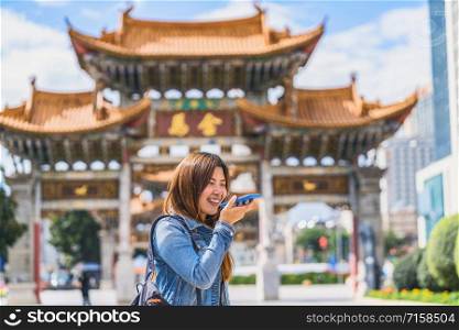 Asian traveler woman using smart mobile phone for voice command recorder to translate when travelling over the Jinbi square, Kunming, China, travel and tourism, famous place and landmark concept