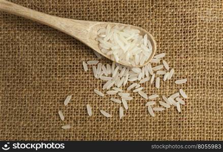 Asian uncooked white rice in a wooden spoon on a background of rough cloth
