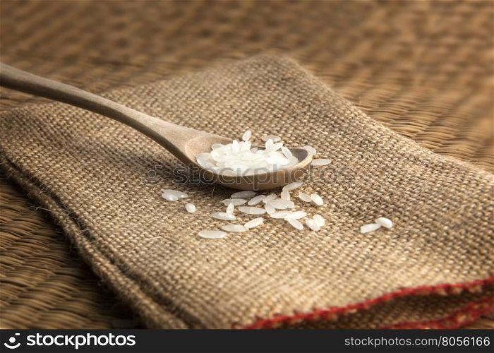 Asian uncooked white rice in a wooden spoon on a background of rough cloth