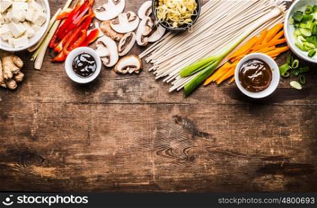 Asian vegetarian cooking ingredients for stir fry with tofu, noodles, ginger, cut vegetables, Sprout,green onion , lemongrass, hoisin and austern sauce on wooden rustic background, top view, border