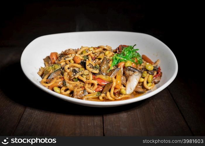 Asian vegetarian food udon noodles with shiitake mushrooms, sesame and pepper close-up on a plate on the wooden table. High quality photo. Asian vegetarian food udon noodles with shiitake mushrooms, sesame and pepper close-up on a plate on the wooden table.