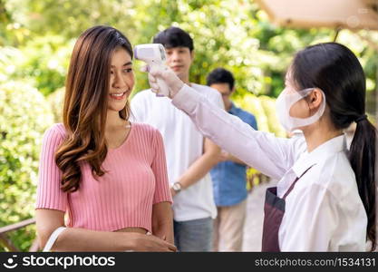 Asian waitress with face mask take temperature customer before getting in restaurant with social distance queue in line. Restaurant New normal restaurant concept after coronavirus covid-19 pandemic.