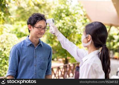 Asian waitress with face mask take temperature customer before getting in restaurant. Restaurant New normal restaurant lifestyle concept after coronavirus covid-19 pandemic.