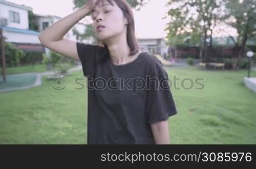 Asian wiping sweat from face resting during exercise, running on green grass inside the park, during sunset, blood flow circulation system, Relaxing muscle before work out, injury prevention