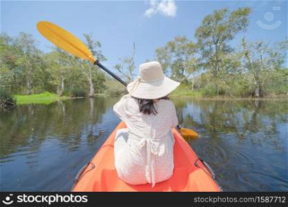 Asian woman, a tourist, paddling a boat, canoe or kayak with trees in Rayong Botanical Garden, Paper Bark Tropical Forest in national park in Thailand. People lifestyle adventure activity recreation.