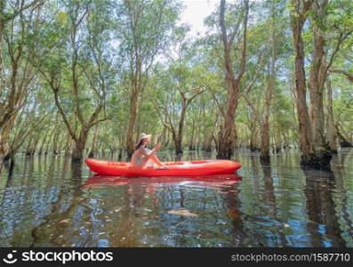 Asian woman, a tourist, reading a book on a boat, canoe or kayak with trees in Rayong Botanical Garden, Old Paper Bark Forest, tropical forest in national park in Thailand. People lifestyle activity.
