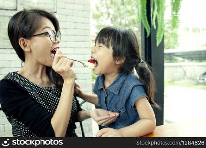asian woman and daughter eating strawberry cake in home living room