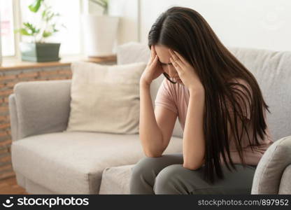 Asian woman are holding their hands to the head in pain on the sofa at home, Young women have severe headaches from migraines, Health and illness concept