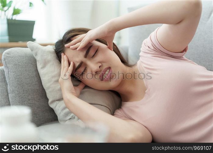 Asian woman are holding their hands to the head in pain sleeping on sofa at home, Young women have severe headaches from migraines, Health and illness concept