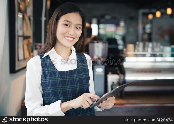 Asian woman barista smiling with tablet in her hand,Female employees are taking orders from online customers.,Warm photos at the coffee shop