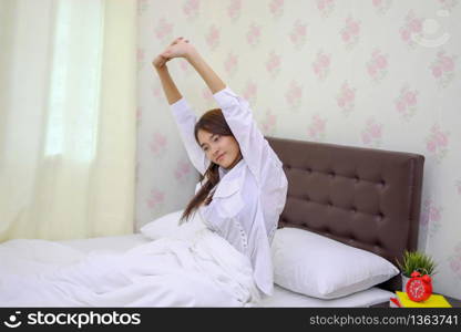 Asian woman Beautiful young smiling woman sitting on bed and stretching in the morning at bedroom after waking up in her bed fully rested