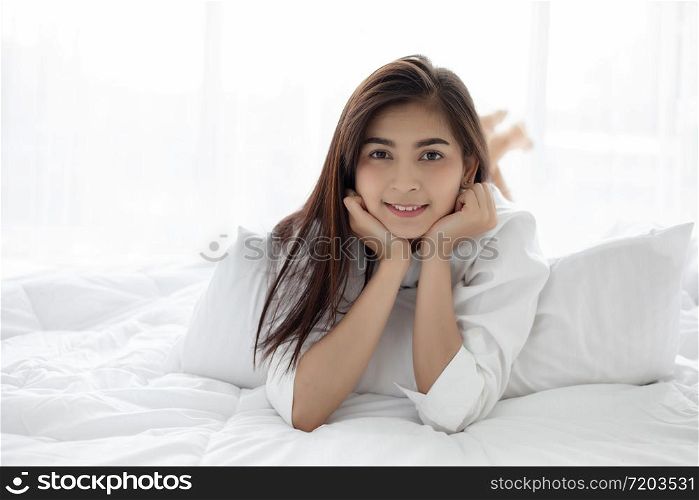 Asian woman Beautiful young smiling woman sitting on bed and stretching in the morning at bedroom after waking up in her bed fully rested and open the curtains in the morning to get fresh air.