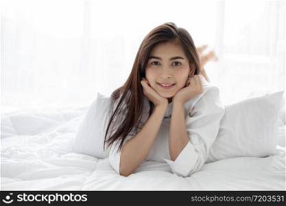Asian woman Beautiful young smiling woman sitting on bed and stretching in the morning at bedroom after waking up in her bed fully rested and open the curtains in the morning to get fresh air.