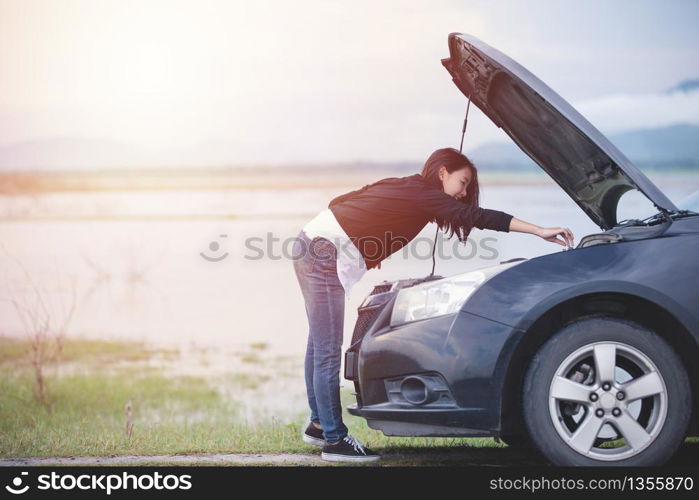 Asian woman checking broken down car on street