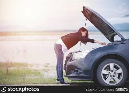 Asian woman checking broken down car on street