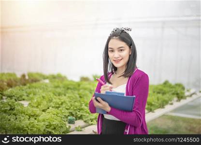 Asian woman checking report organic hydroponic fresh vegetables produce in farm, agriculture business, healthy food concept. agriculture business, healthy food concept