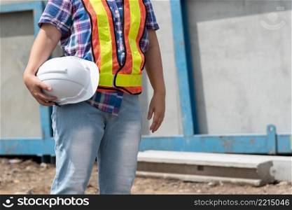 Asian woman civil construction engineer worker or architect with helmet and safety vest happy working at a building or construction site. Woman construction engineer at construction site