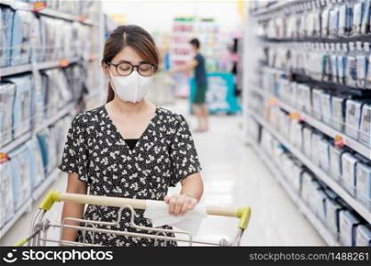 Asian woman cleaning surface of shopping cart by wet wipe in supermarket or grocery, protect coronavirus inflection. Hygiene, new normal and life after covid-19 pandemic