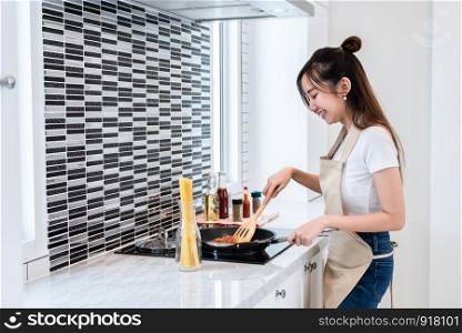 Asian woman cooking spaghetti in kitchen happily. People and lifestyles concept. Food and drink theme. Interior decoration and housework theme.