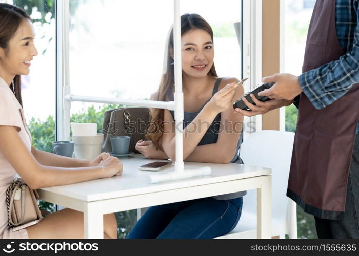 Asian woman customer hold contactless credit card for making online payment after eating out in new normal social distance restaurant. Online contactless and technology concept.