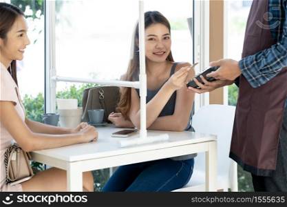 Asian woman customer hold contactless credit card for making online payment after eating out in new normal social distance restaurant. Online contactless and technology concept.