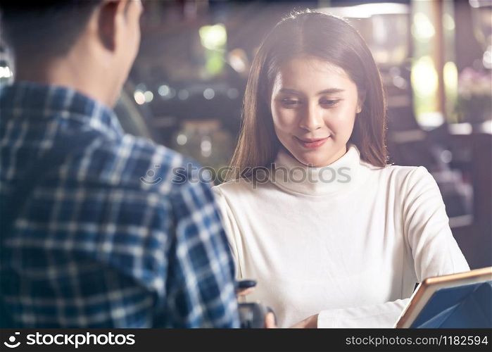 Asian woman customer using mobile phone scane QR code on credit card reader EDC machine to pay a waiter for coffee purchase at table in cafe.