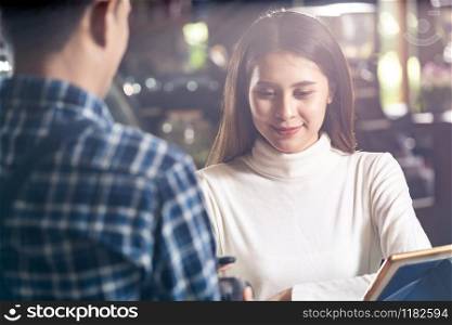 Asian woman customer using mobile phone scane QR code on credit card reader EDC machine to pay a waiter for coffee purchase at table in cafe.