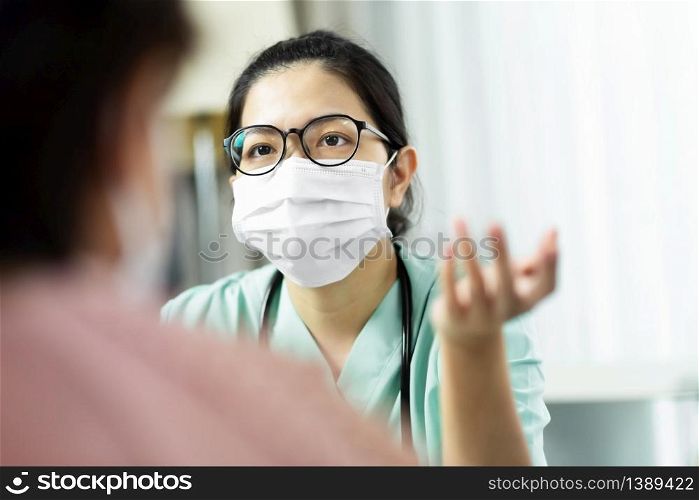 Asian woman Doctor in green uniform wear eyeglasses and surgical mask talking, consulting and giving advice to Elderly female patient at the hospital. Symptoms, Disease, Flu, Covid-19, Coronavirus.