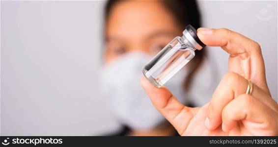 Asian woman doctor wearing surgical protective cloth face mask against coronavirus her hold ampoule bottle vaccine focus on glass transparent, studio shot isolated white background, COVID-19 concept