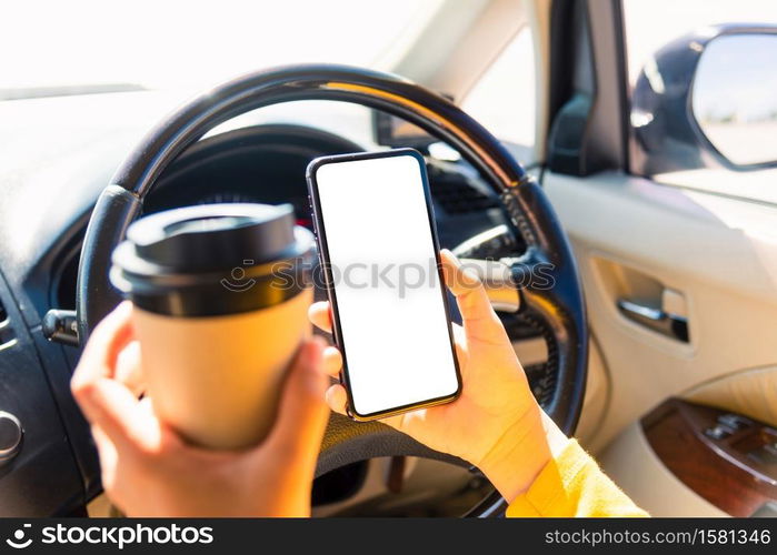 Asian woman drinking hot coffee takeaway cup inside a car and using smartphone blank screen while driving the car in the morning during going to work on highway, Transportation and vehicle concept