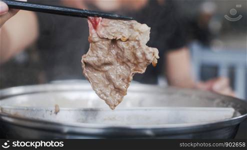 Asian woman eating hot pot in japanese restaurant, young female holding sliced beef meat by chopsticks eat shabu in lunch time. Lifestyle women eating food concept.