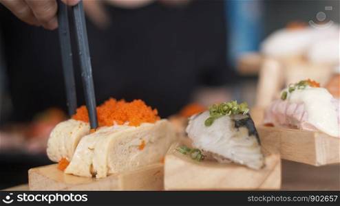 Asian woman eating sushi in japanese restaurant, young female holding chopsticks and eating salmon sushi in lunch time in summer. Lifestyle women eating traditional food concept.