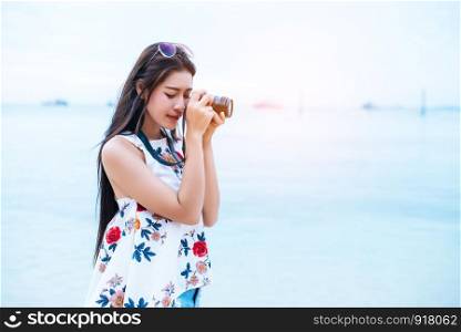 Asian woman enjoy take photo by digital camera at beach. Single and lonely woman concept. Happiness and Lifestyle concept. Beauty and Nature theme. Ocean and sea background. Technology and woman day