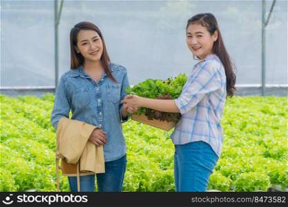 Asian woman farmer holding a vegetable basket of fresh vegetable salad on organic farm and shaking hands with a customer. Concept of agriculture organic for health, Vegan food, and Small business.