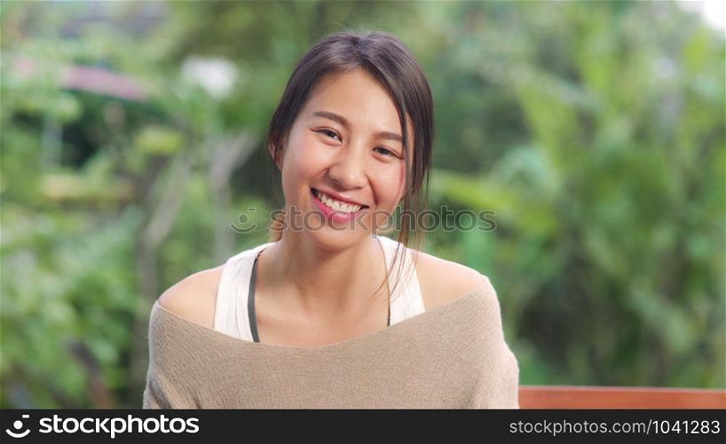 Asian woman feeling happy smiling and looking to camera while relax on table in garden at home in the morning. Lifestyle women relax at home concept.