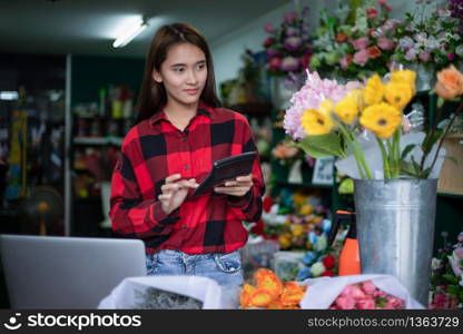 Asian Woman Florist Small Business Flower Shop Owner and She is using her Calculator and laptop to take orders for her store.