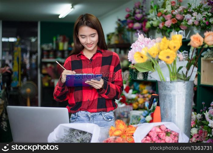 Asian Woman Florist Small Business Flower Shop Owner and She is using her telephone and laptop to take orders for her store.