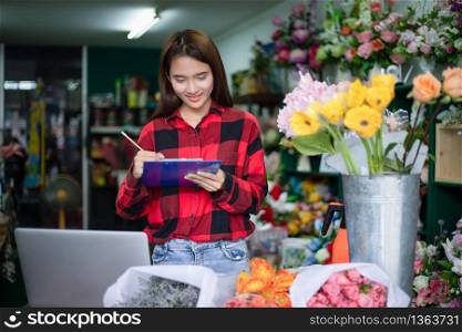 Asian Woman Florist Small Business Flower Shop Owner and She is using her telephone and laptop to take orders for her store.