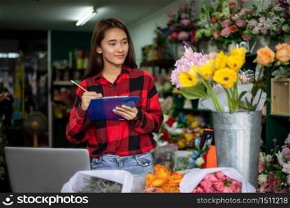 Asian Woman Florist Small Business Flower Shop Owner working and Holding A Clipboard Writing to take orders for her store.