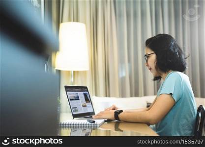 Asian woman Freelancer Designer wear eyeglasses working on laptop computer in night time. Young Female student studying and doing online learning at home. Social distancing, New normal life concept.