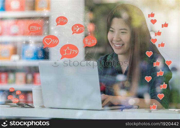 Asian woman hand using laptop to check social network application with number of Like, Love, comment, people and fovorite icon at desk beside glass in coffee shop, Social media concept,