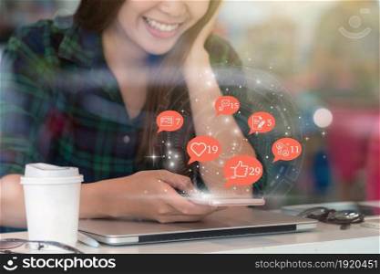 Asian woman hand using mobile phone to check social network application with number of Like, Love, comment, people and fovorite icon at desk beside glass in coffee shop, Social media concept,