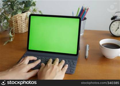 Asian woman hands are using tablet has a green screen on the desk by the window.