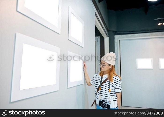 Asian woman hold camera at art gallery collection in front framed paintings pictures on wall and looking, Photographer visit at photo frame to leaning against at show exhibit artwork gallery picture