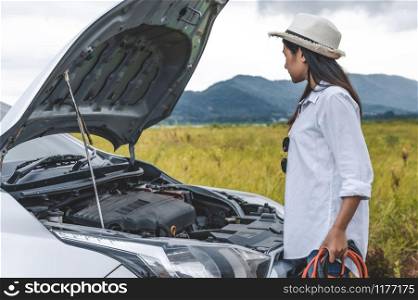 Asian woman holding battery booster cable copper wire for repairing breakdown broken car by connect with red and black line to electric terminal by herself. Car maintenance and transportation concept