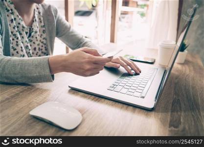 Asian woman holding credit card paying for shopping in computer laptop on wooden table