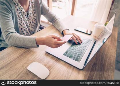 Asian woman holding credit card paying for shopping in computer laptop on wooden table